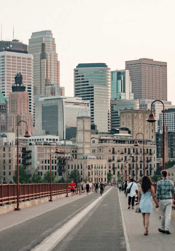 A cityscape with a bridge and people walking on it at The Bessemer at Seward Commons Apartments, MN, 55404