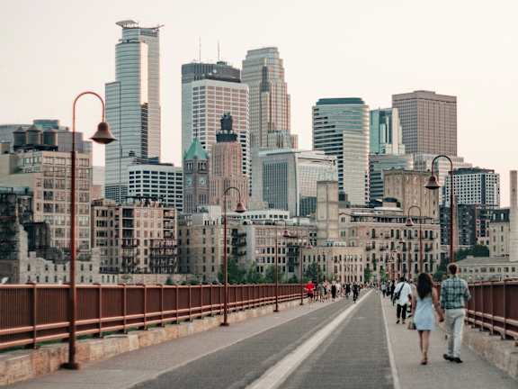 A couple walking on a bridge with a city skyline in the background.