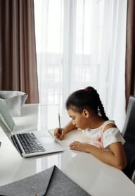 A young girl is writing at a desk with a laptop and a tablet. at Notch 8, Tacoma, Washington