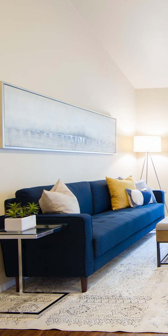 A living room with a blue couch, a coffee table, and a painting on the wall.