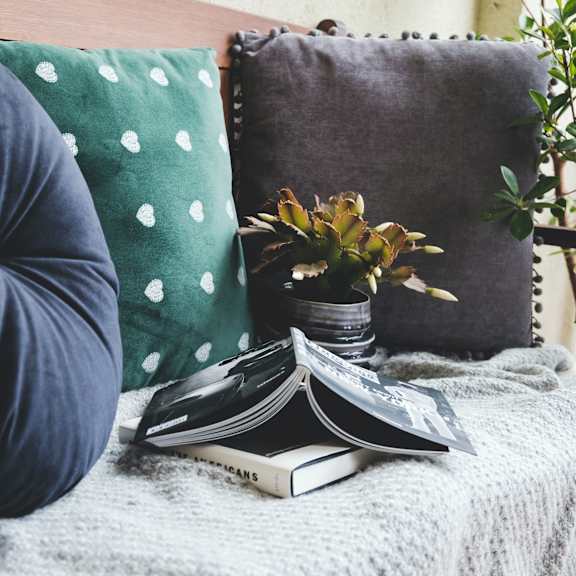 A person is sitting on a couch with a green pillow and a white lantern beside them.