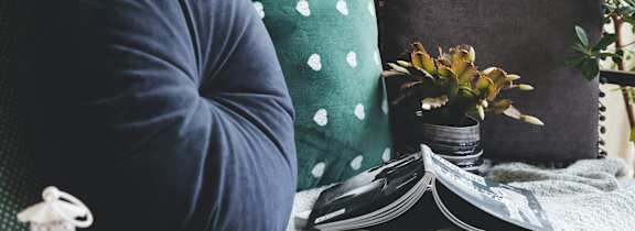 A person is sitting on a couch with a green pillow and a white lantern beside them.