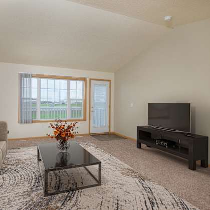 A living room with a couch, coffee table, and tv with an entry door and a window. West Fargo, ND Charleswood Townhomes.