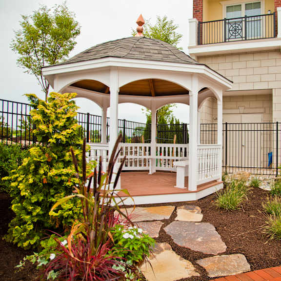A gazebo is surrounded by a garden and a black fence.