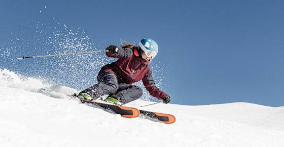 A skier is in action, kicking up snow as they descend a slope.