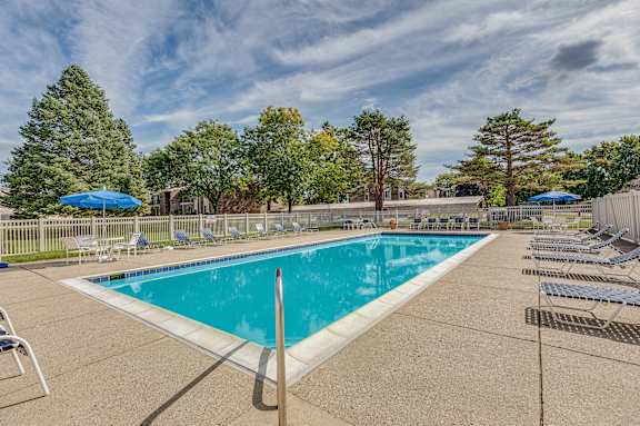A large outdoor swimming pool surrounded by trees and lounge chairs.