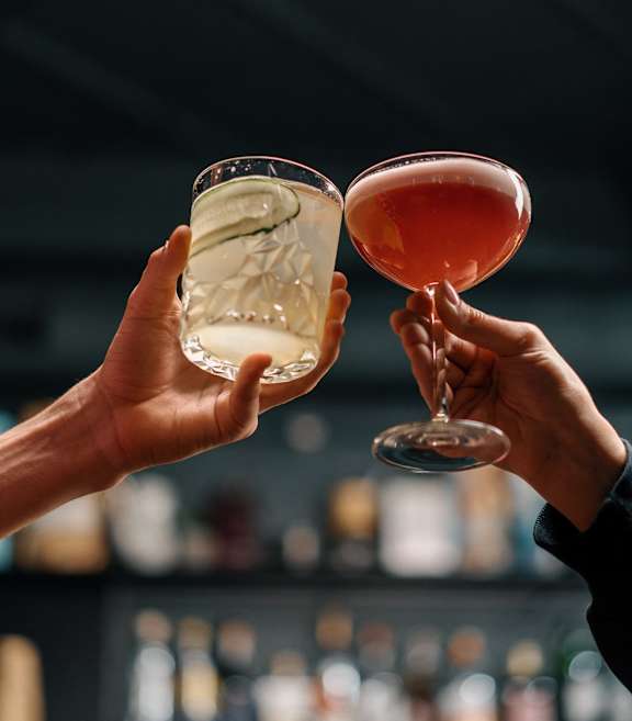 Two people toasting with drinks in a bar setting.