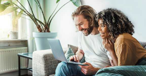a couple sitting on a couch looking at a laptop