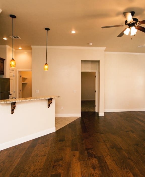 an empty living room with a ceiling fan and a kitchen