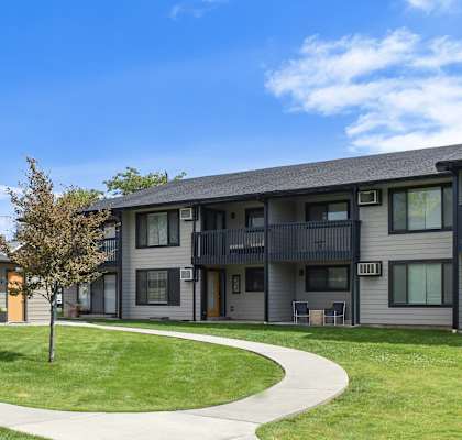 an exterior view of an apartment building with a green lawn and sidewalk