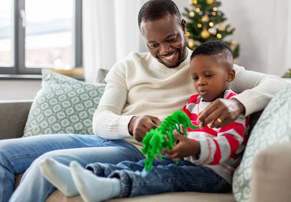 A man and a child are sitting on a couch playing with a green toy.
