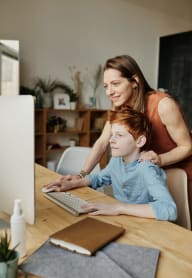 a mother helping her son using a computer at a desk