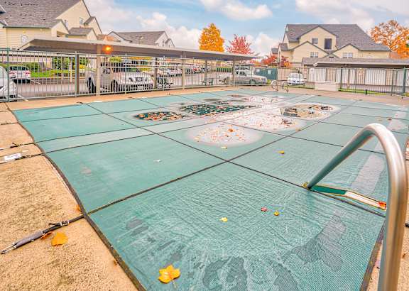 A green tarp covers a swimming pool in a backyard.