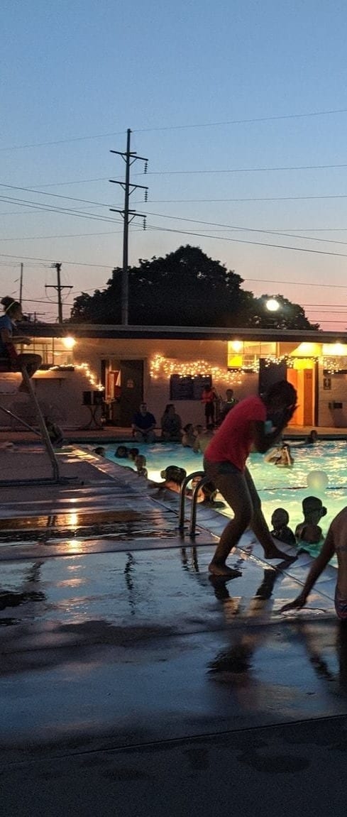 a group of people sitting in front of a swimming pool at night