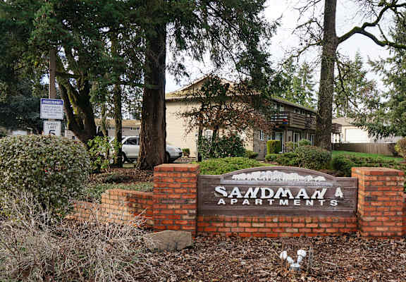 A sign for Saadman Apartments is surrounded by a brick wall and shrubbery.