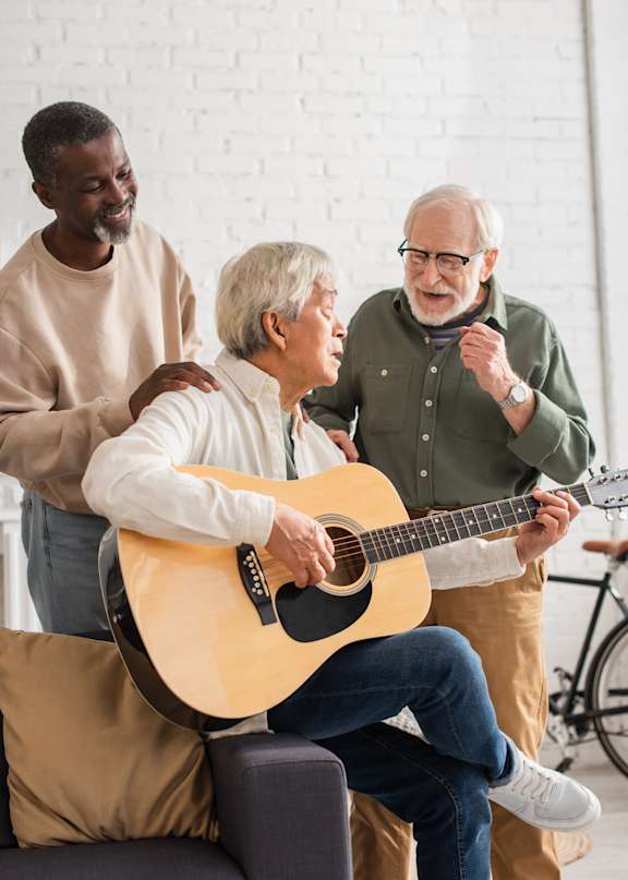 A man is playing guitar while two other men listen.