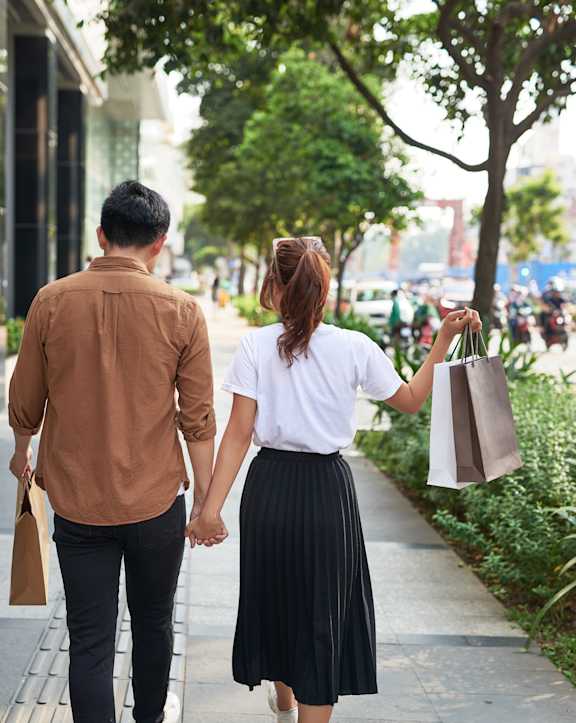 A man and a woman are walking down a sidewalk holding hands.