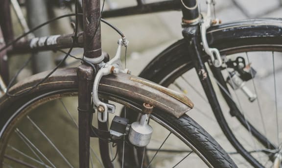 a bicycle parked on the street with its front tire rusty