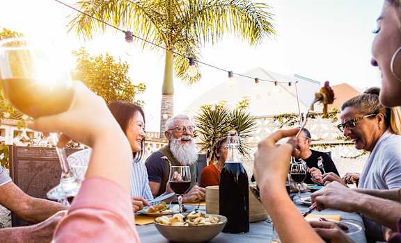 a group of people sitting around a table eating food and drinking wine