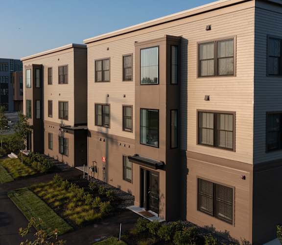 A row of modern townhouses with a sidewalk and landscaping in front.