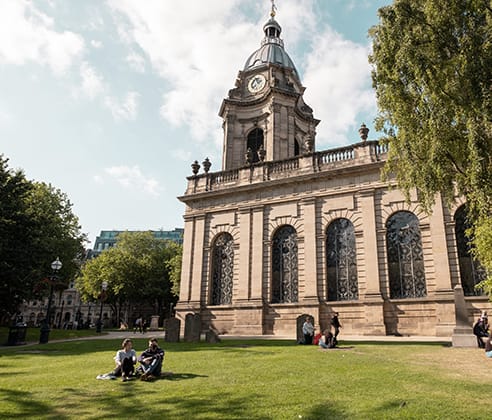 people sitting on the grass in front of a building with a clock tower