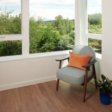 a chair with an orange pillow sitting in a room with windows