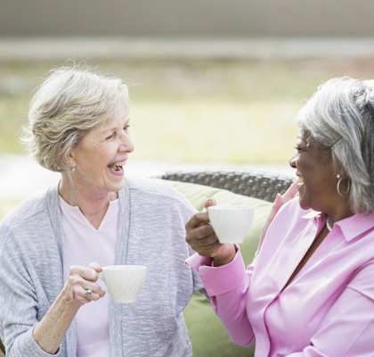 two older women laughing and holding cups of coffee at Windsor Crossing Senior, Suitland, MD