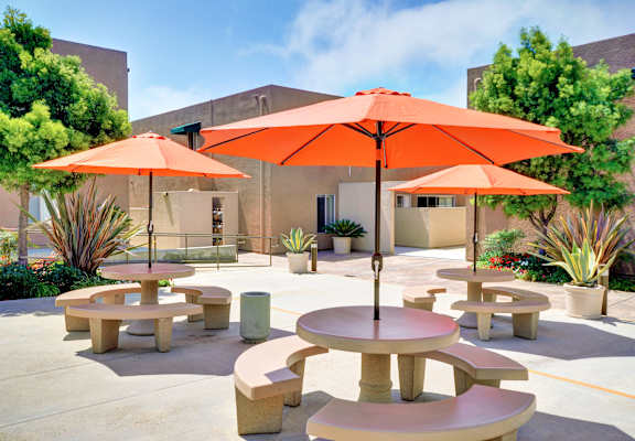 A sunny day at a courtyard with orange umbrellas and tables at Village Square, La Jolla