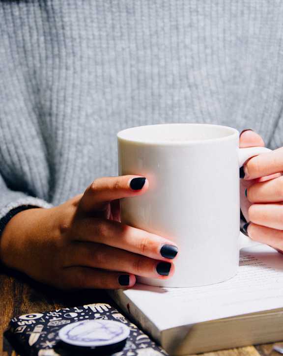 A person in a grey sweater is holding a white mug.
