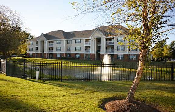 A tree is planted in front of a building with a black fence around it.