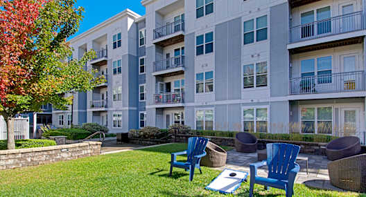 A sunny day at a grassy courtyard with blue chairs and a white building in the background.