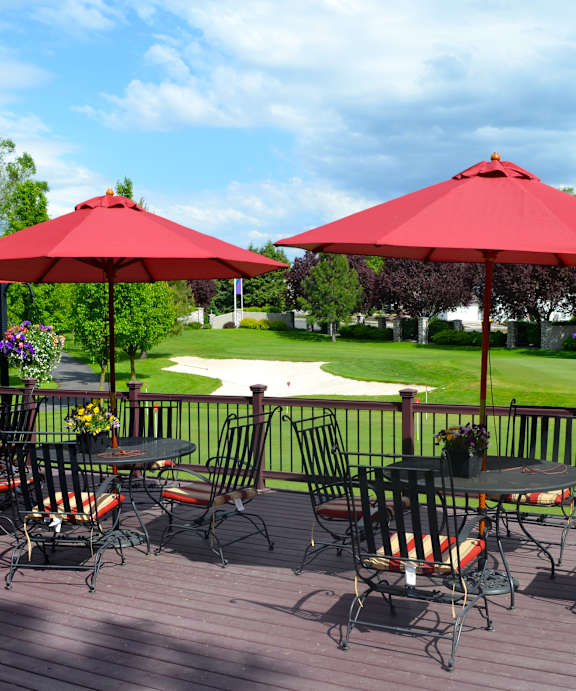 A patio with red umbrellas and chairs overlooking a green lawn.