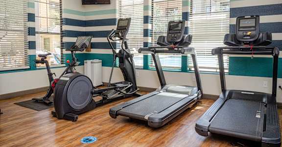 A room with a treadmill, elliptical trainer and a stationary bike.