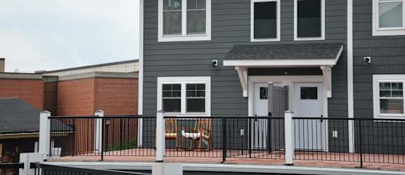 the front of a house with a balcony and a brick building in the background