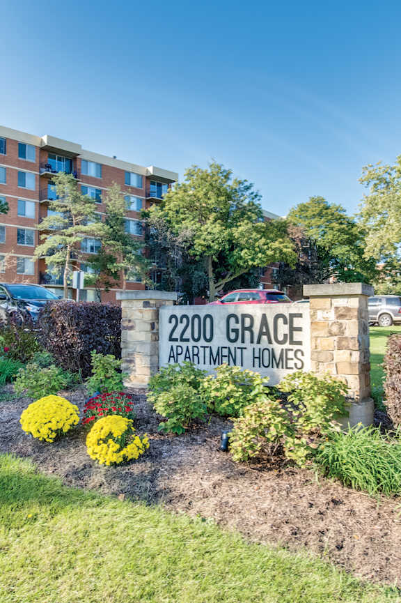A sign for 2200 Grace Apartment Homes is surrounded by flowers and greenery.