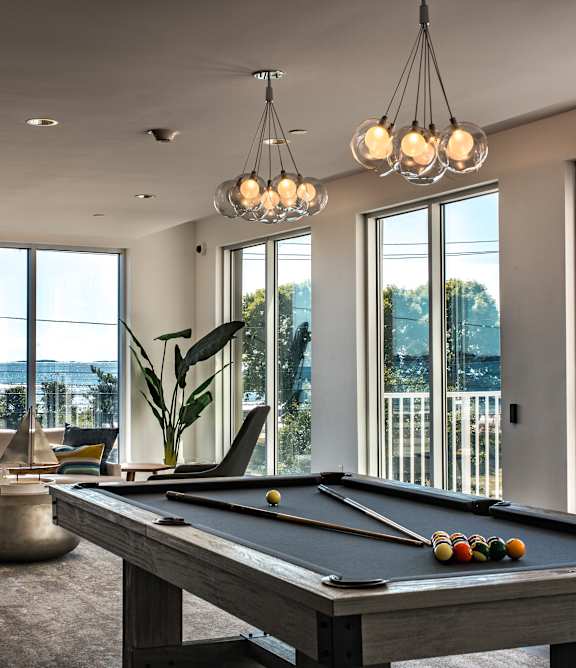 Game room with a gray pool table, pendant lights and floor-to-ceiling windows showing an ocean view