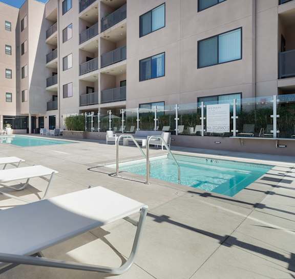 A pool area with sun loungers and a building in the background at Wilshire Valencia Apartment, California