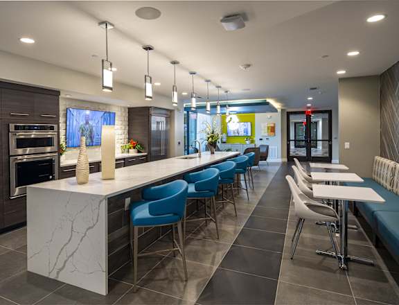 A modern kitchen with a long white island and blue chairs.