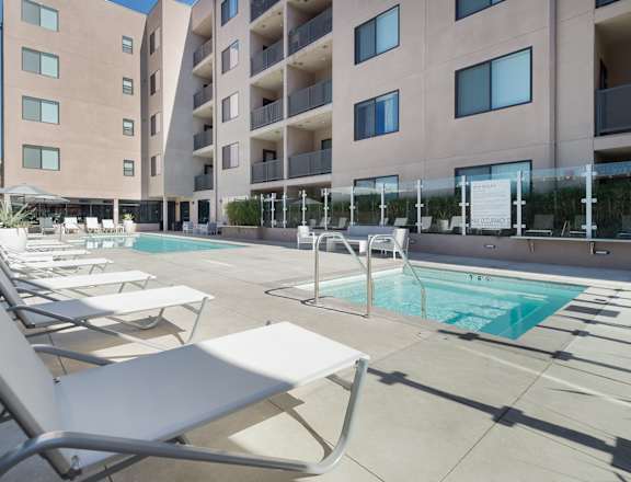 A pool area with sun loungers and a building in the background at Wilshire Valencia Apartment, California