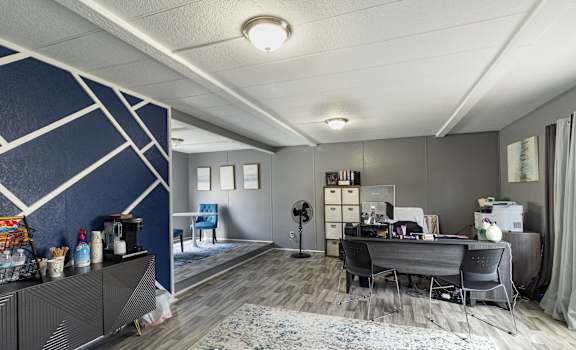 A room with a desk, chairs, and a fan.
