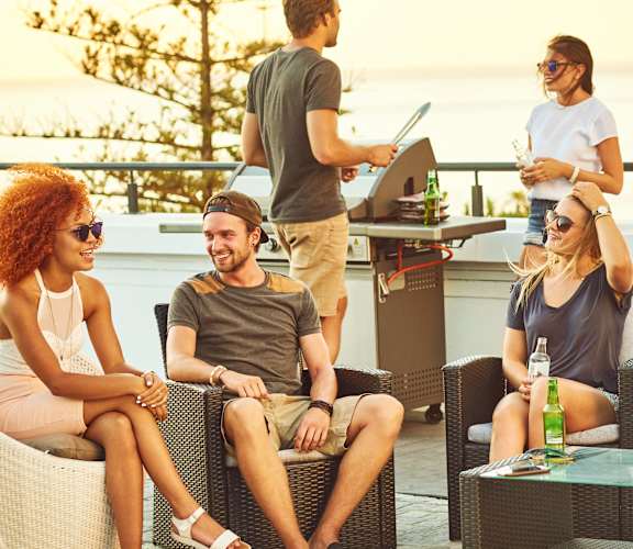 A group of people are sitting and standing around a table on a patio.