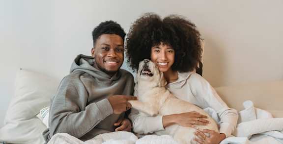 a man and woman sitting on a bed holding a dog