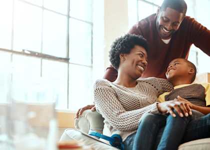A family of three is sitting on a couch in a bright room.