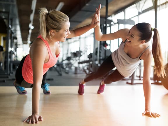 two women giving each other a high five while doing push ups in a gym