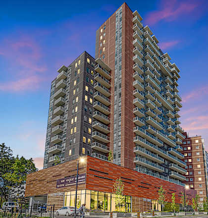 A tall building with a red brick facade stands in front of a sky with clouds.