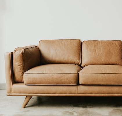 A tan leather couch with wooden legs sits in a room.
