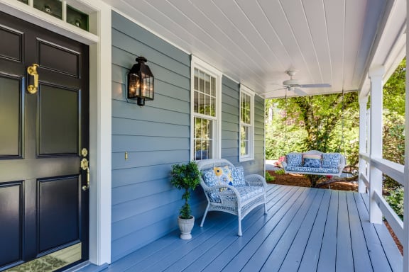 front porch of a blue house with two chairs and a black door