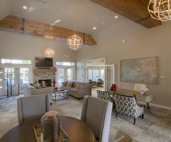The amazing resident lounge with a fireplace, couches, decorations, large windows and glass doors to the outside, plush chairs, and coffee tables at Villas at Preston Lakes Apartment Homes. 