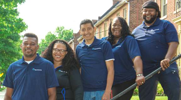 Five people in blue shirts stand in front of a building.