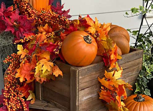 A wooden crate filled with pumpkins and leaves.